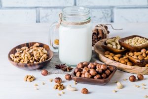 Vegan milk from nuts in glass jar with various nuts on white wooden background