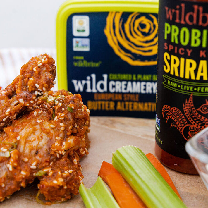 2 chicken wings on a plate with celery and carrot sticks with wild creamery butter and sriracha